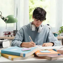 Un chico con auriculares se concentra en sus estudios, rodeado de libros y un casco de RV. ¡Yo también!