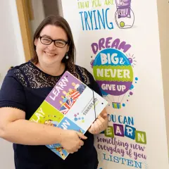 Mujer sonriente con carpeta de aprendizaje con diseño de globos y banderas.