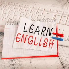 Cuaderno con "LEARN ENGLISH" escrito a mano, sobre un teclado. Una lista de palabras en inglés para aprender.
