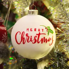 Adorno blanco con "Merry Christmas" en rojo. Un muñeco de nieve tejido y guirnaldas brillantes completan la escena festiva.