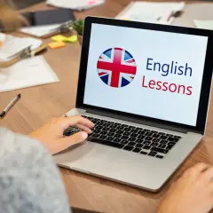 Persona aprende inglés en línea. La pantalla muestra "English Lessons" y la bandera del Reino Unido.