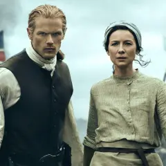 Jamie y Claire, protagonistas de series inglesas antiguas, se preparan para la batalla. Banderas ondean al fondo.