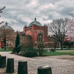 Edificio de ladrillo rojo con cúpulas, rodeado de árboles en flor. Un lugar ideal para estudiar en universidades en Inglaterra para extranjeros.