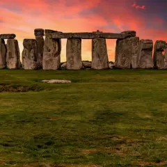Las imponentes piedras de Stonehenge en Inglaterra se alzan contra un cielo crepuscular de tonos naranjas y rojizos, un misterio ancestral bajo la luz del atardecer.