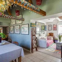 Interior de una casa típica inglesa con decoración colorida y vintage. Se ve un comedor con mantel a rayas y un salón con sofá, alfombra y cuadros.