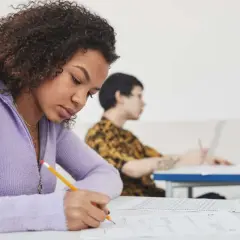 Chica concentrada escribiendo en un examen, preparándose para su b1 aptis.