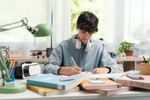 Un chico con auriculares se concentra en sus estudios, rodeado de libros y un casco de RV. ¡Yo también!