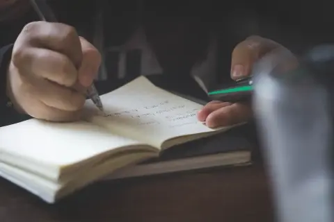 Mano escribiendo en un cuaderno. Quizás anotando **palabras homógrafas** para un estudio.