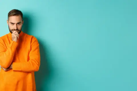 Hombre con suéter naranja, pensativo, reflexionando sobre la diferencia entre fun y funny.