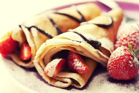 Cremosas crepas rellenas de fresas y bañadas en chocolate, perfectas para celebrar el pancake day. Espolvoreadas con azúcar glas.