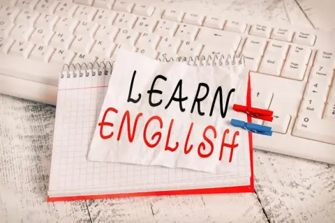 Cuaderno con "LEARN ENGLISH" escrito a mano, sobre un teclado. Una lista de palabras en inglés para aprender.