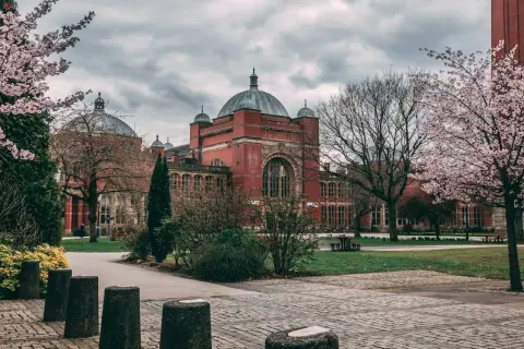 Edificio de ladrillo rojo con cúpulas, rodeado de árboles en flor. Un lugar ideal para estudiar en universidades en Inglaterra para extranjeros.