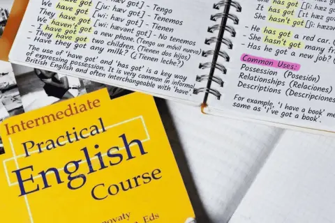 Cuaderno con apuntes de inglés sobre "have got", un libro de texto "Practical English Course" y un ejemplo de posesión: "He has got a red car".