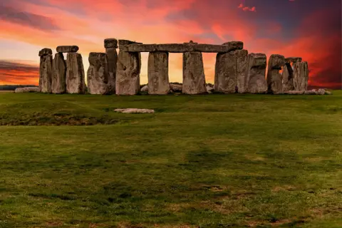 Las imponentes piedras de Stonehenge en Inglaterra se alzan contra un cielo crepuscular de tonos naranjas y rojizos, un misterio ancestral bajo la luz del atardecer.