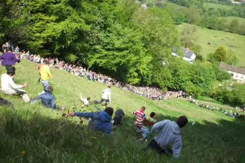 Gente rodando colina abajo en una carrera de cheese rolling.