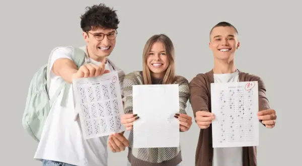 Tres estudiantes sonríen mostrando sus hojas de respuestas con puntuaciones aptis de A+.