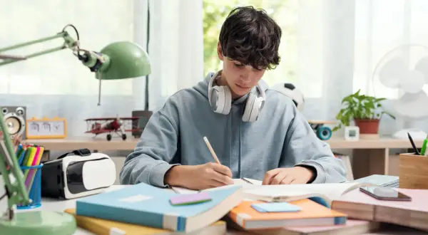 Un chico con auriculares se concentra en sus estudios, rodeado de libros y un casco de RV. ¡Yo también!