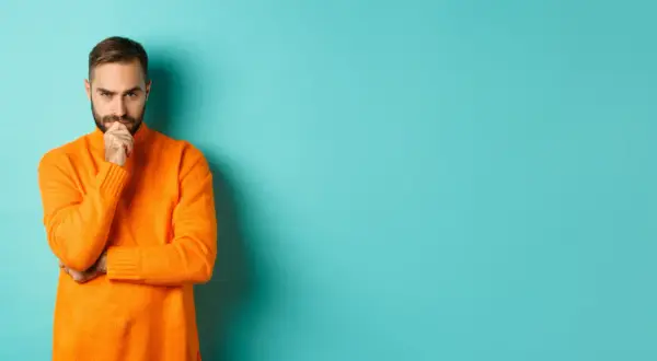 Hombre con suéter naranja, pensativo, reflexionando sobre la diferencia entre fun y funny.