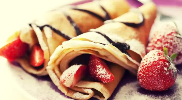 Cremosas crepas rellenas de fresas y bañadas en chocolate, perfectas para celebrar el pancake day. Espolvoreadas con azúcar glas.
