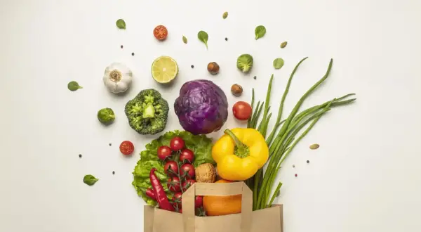 Bolsa de papel llena de verduras frescas: brócoli, col morada, pimientos, cebolletas, tomates, chiles, ajo, limón y una naranja. ¡Perfecto para 100 comidas!