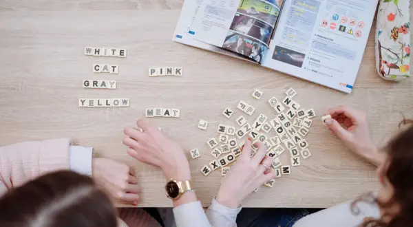 Estudiantes aprenden c1 vocabulary con fichas de letras y un libro de inglés.