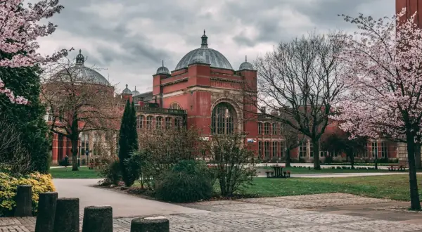 Edificio de ladrillo rojo con cúpulas, rodeado de árboles en flor. Un lugar ideal para estudiar en universidades en Inglaterra para extranjeros.