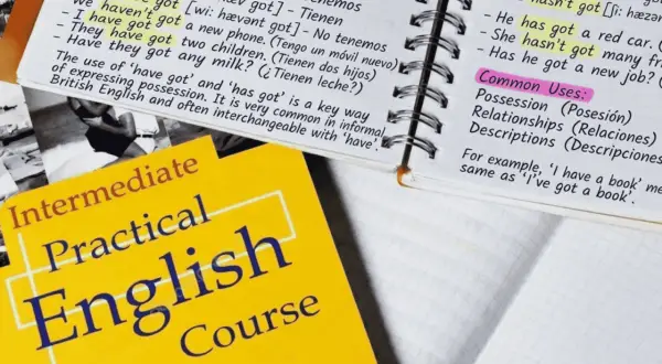 Cuaderno con apuntes de inglés sobre "have got", un libro de texto "Practical English Course" y un ejemplo de posesión: "He has got a red car".
