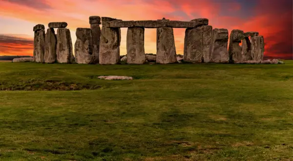 Las imponentes piedras de Stonehenge en Inglaterra se alzan contra un cielo crepuscular de tonos naranjas y rojizos, un misterio ancestral bajo la luz del atardecer.