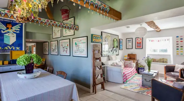 Interior de una casa típica inglesa con decoración colorida y vintage. Se ve un comedor con mantel a rayas y un salón con sofá, alfombra y cuadros.