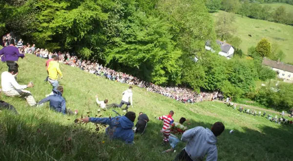 Gente rodando colina abajo en una carrera de cheese rolling.