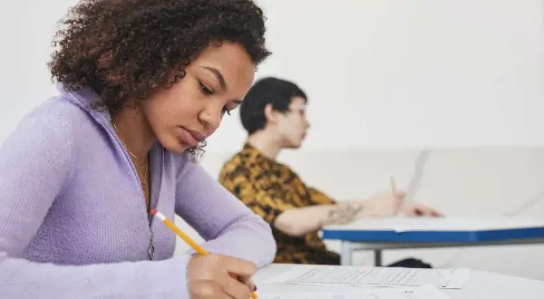 Chica concentrada escribiendo en un examen, preparándose para su b1 aptis.