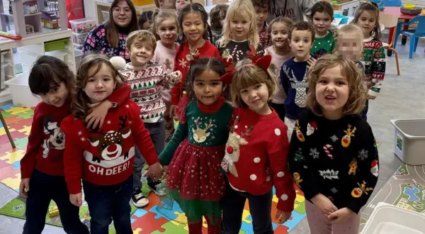 Niños y adultos celebran el jumper day con suéteres festivos en un aula. ¡Felices fiestas!