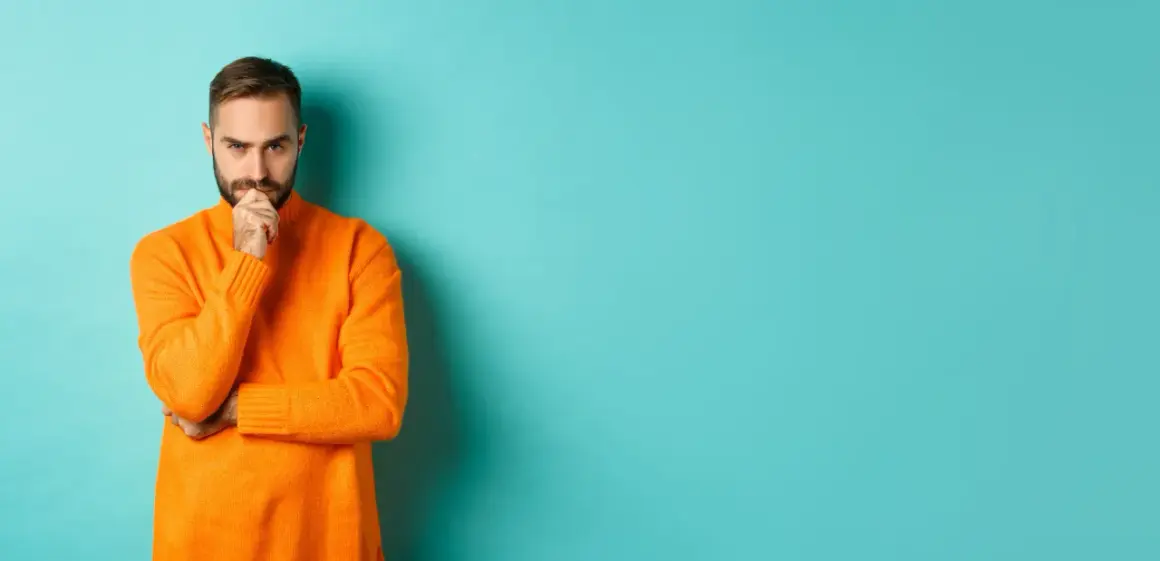 Hombre con suéter naranja, pensativo, reflexionando sobre la diferencia entre fun y funny.