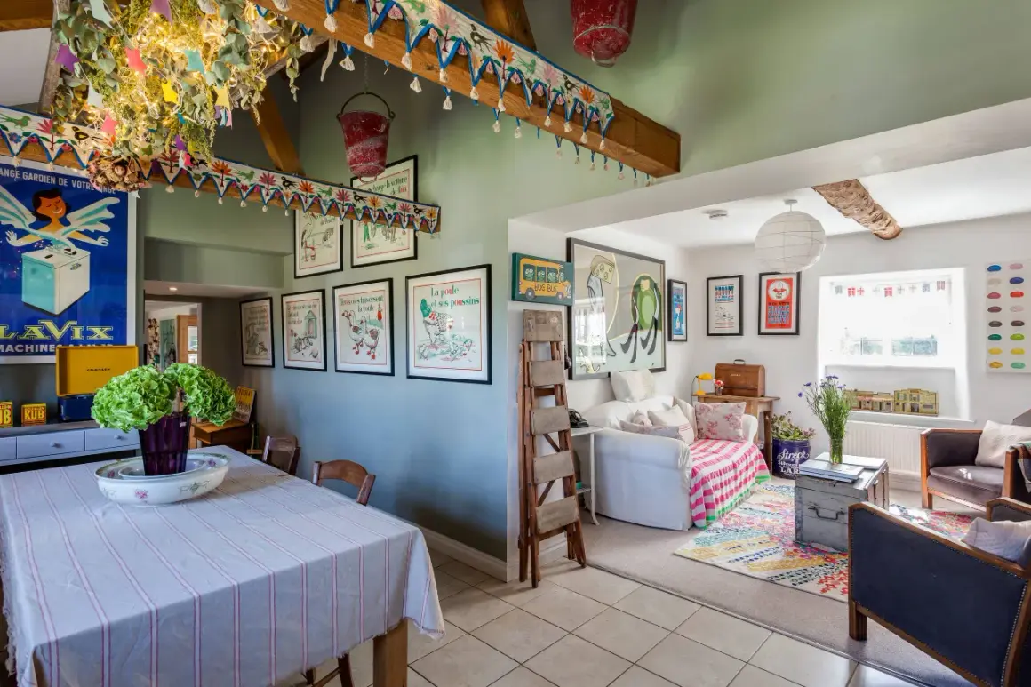 Interior de una casa típica inglesa con decoración colorida y vintage. Se ve un comedor con mantel a rayas y un salón con sofá, alfombra y cuadros.