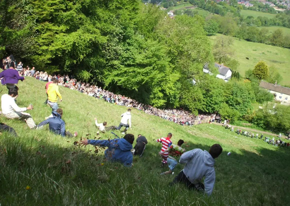 Gente rodando colina abajo en una carrera de cheese rolling.