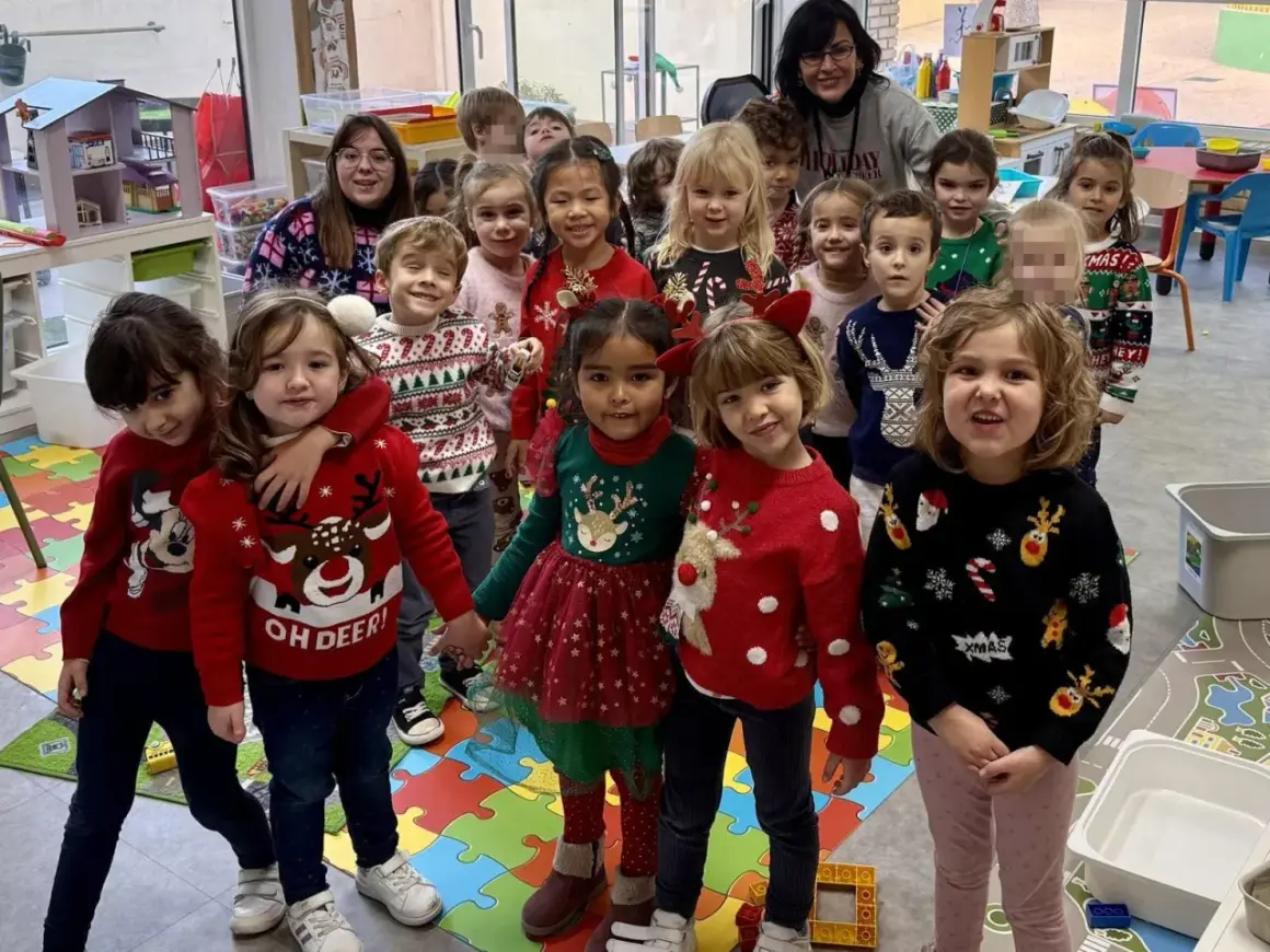 Niños y adultos celebran el jumper day con suéteres festivos en un aula. ¡Felices fiestas!