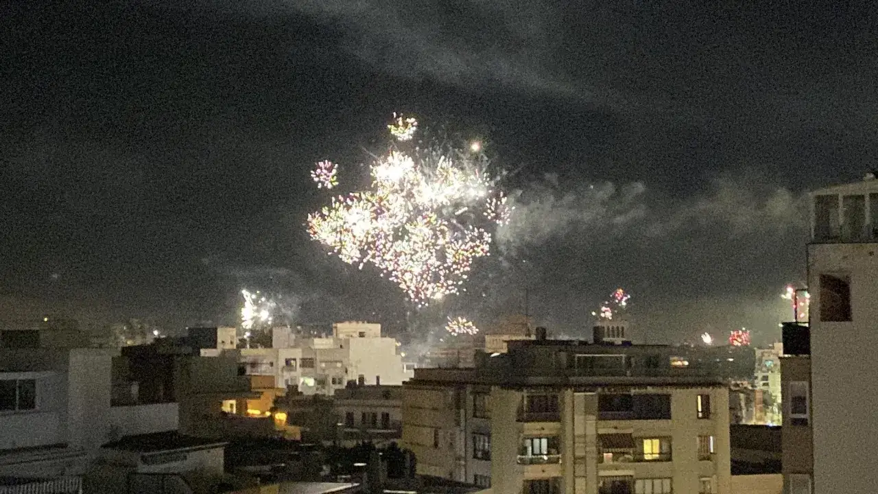 Fuegos artificiales iluminan el cielo nocturno sobre edificios, celebrando el Año Nuevo y los nuevos propósitos.