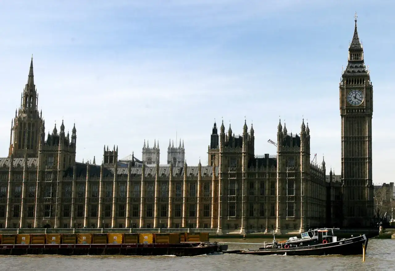 El icónico reloj Big Ben se alza junto al Palacio de Westminster, con barcazas navegando por el río Támesis.
