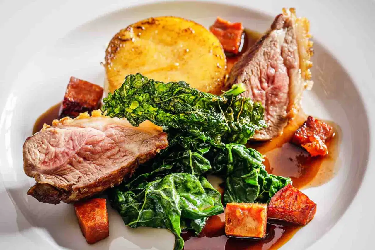 Delicioso plato de comida inglesa: jugoso cordero asado, patatas doradas y col rizada, bañado en salsa.