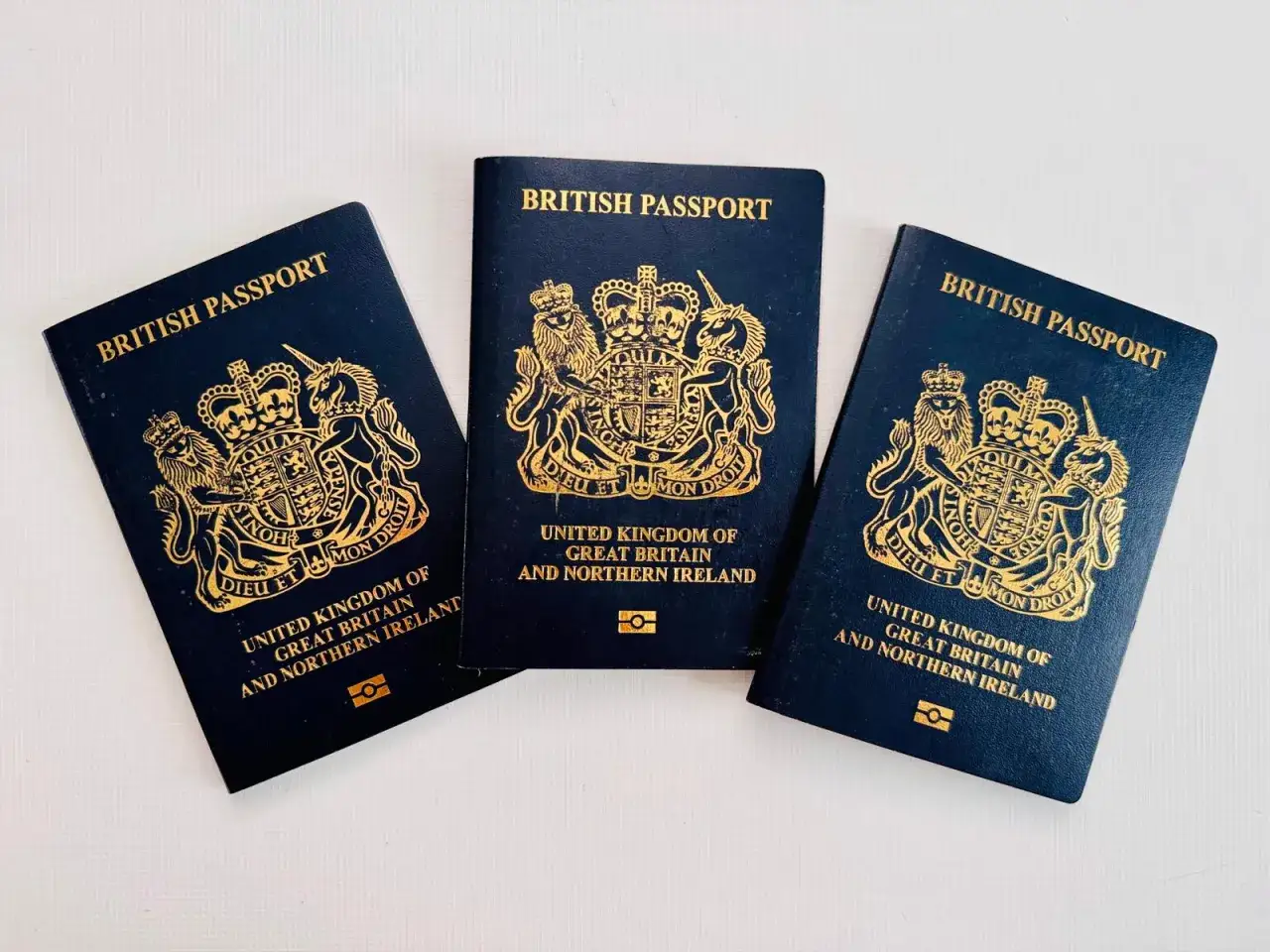 Tres pasaportes brit&aacute;nicos, cada uno con el escudo de armas real dorado, listos para viajes internacionales. Demuestran la nacionalidad de Reino Unido.