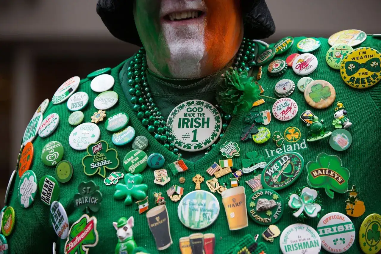 Un hombre celebra cuando es St. Patrick's, cubierto de insignias verdes con tréboles, cerveza y frases irlandesas.