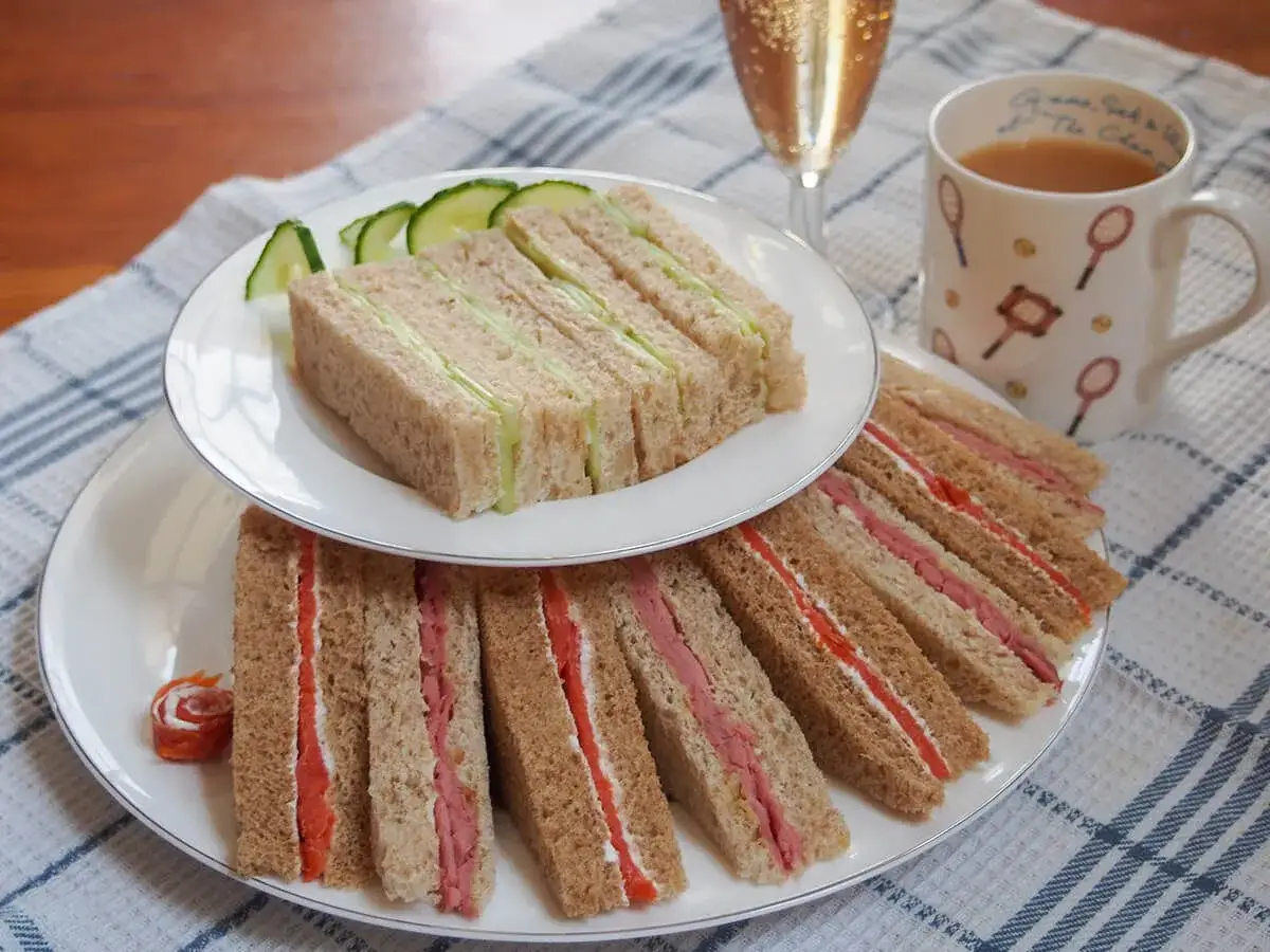 Deliciosos sándwiches de pepino y jamón, listos para la hora del té en Inglaterra. Una taza de té y una copa de champán completan la escena.
