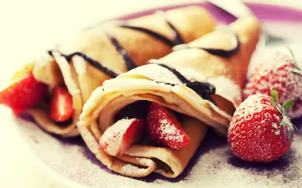 Cremosas crepas rellenas de fresas y bañadas en chocolate, perfectas para celebrar el pancake day. Espolvoreadas con azúcar glas.