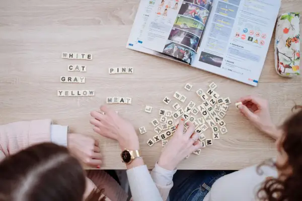 Estudiantes aprenden c1 vocabulary con fichas de letras y un libro de inglés.