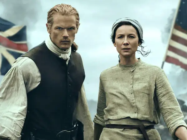 Jamie y Claire, protagonistas de series inglesas antiguas, se preparan para la batalla. Banderas ondean al fondo.