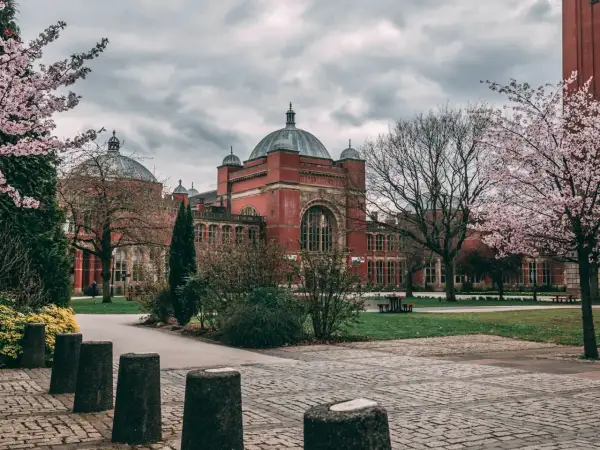 Edificio de ladrillo rojo con cúpulas, rodeado de árboles en flor. Un lugar ideal para estudiar en universidades en Inglaterra para extranjeros.