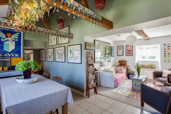 Interior de una casa típica inglesa con decoración colorida y vintage. Se ve un comedor con mantel a rayas y un salón con sofá, alfombra y cuadros.