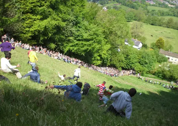 Gente rodando colina abajo en una carrera de cheese rolling.