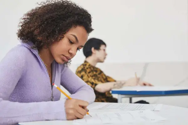Chica concentrada escribiendo en un examen, preparándose para su b1 aptis.